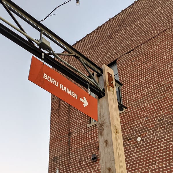 An orange Boru Ramen sign with an arrow points right, against a brick building and sky.