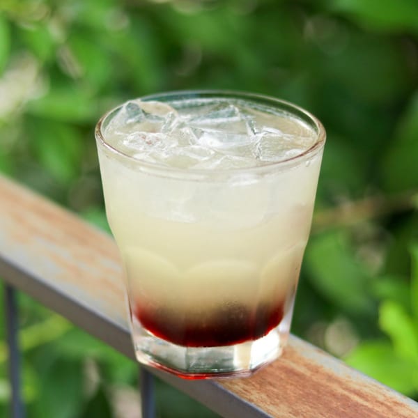 A refreshing Boru Ramen cocktail with a red layer at the bottom and ice, on a wooden railing.