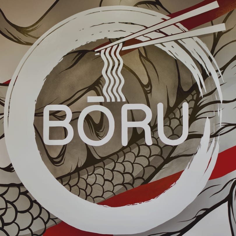 Boru Ramen logo with chopsticks holding noodles inside a white circle, over a dragon pattern.