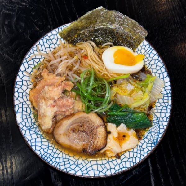 A bowl of Boru Ramen with noodles, pork, egg, seaweed, and vegetables on a dark table.