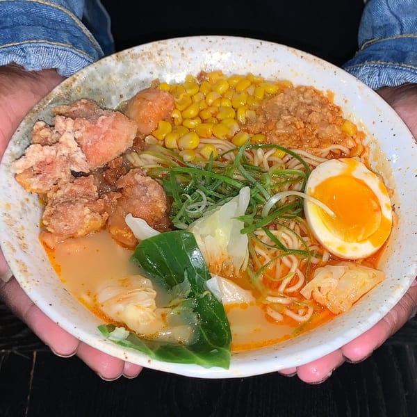 A person holding a bowl of Boru Ramen with fried chicken, corn, scallions, and a soft-boiled egg.