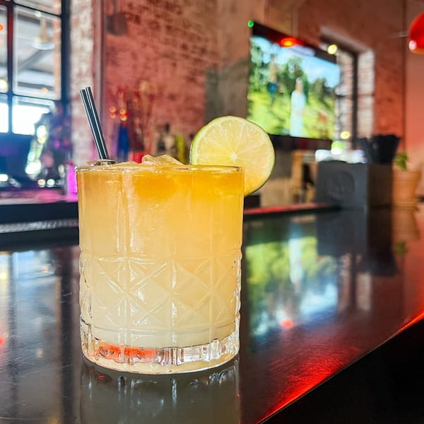 A Boru Ramen cocktail with a lime slice and black straw, on a dark bar with red lighting.