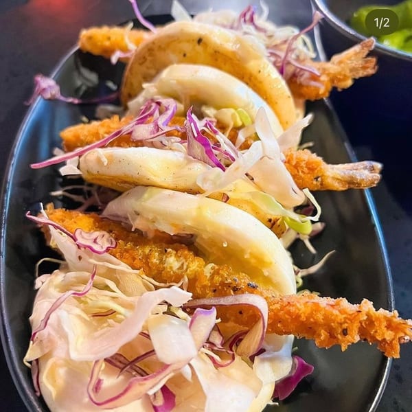 Close-up of Boru Ramen's shrimp tempura tacos with shredded cabbage and sauce on a black plate.