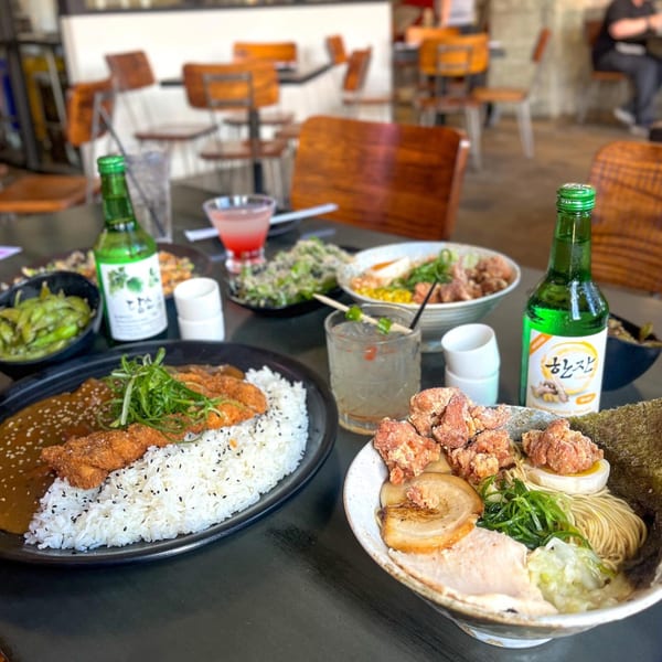Japanese curry with rice and fried chicken, ramen, edamame, and drinks on a table.