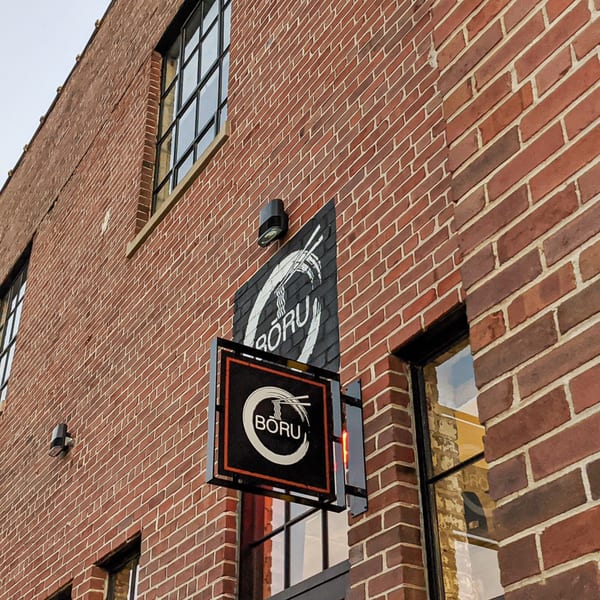 Boru Ramen's black and white sign with chopsticks and noodles, mounted on a brick building.