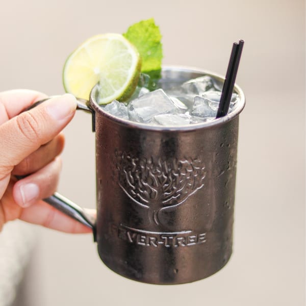 Hand holding a metal mug filled with ice, garnished with lime and mint.