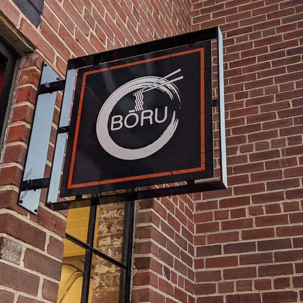 Boru Ramen restaurant sign, black with white logo and orange border, mounted on a brick wall.