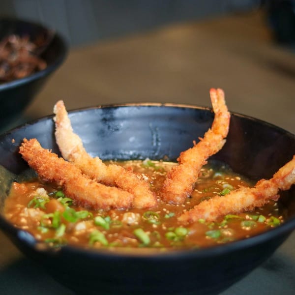 Boru Ramen's Japanese curry with crispy fried shrimp tempura and green onions in a black bowl.