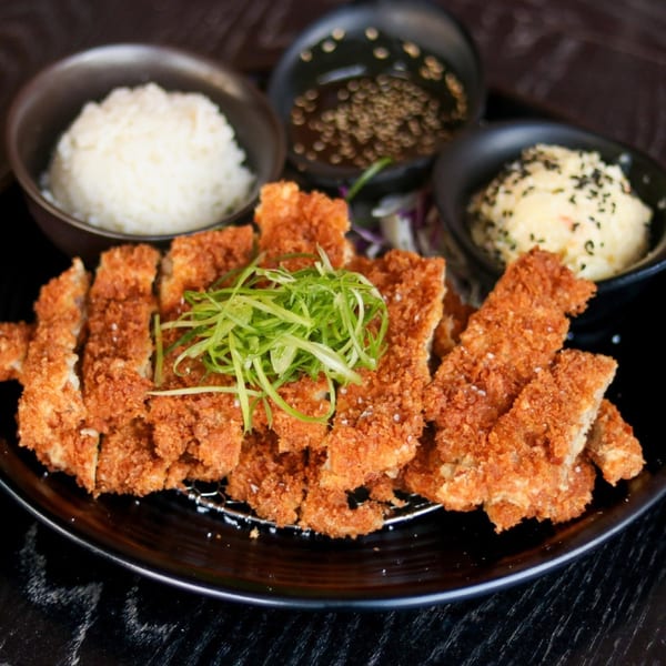 Crispy Boru Ramen chicken katsu with rice, potato salad, and dipping sauce on a black plate.