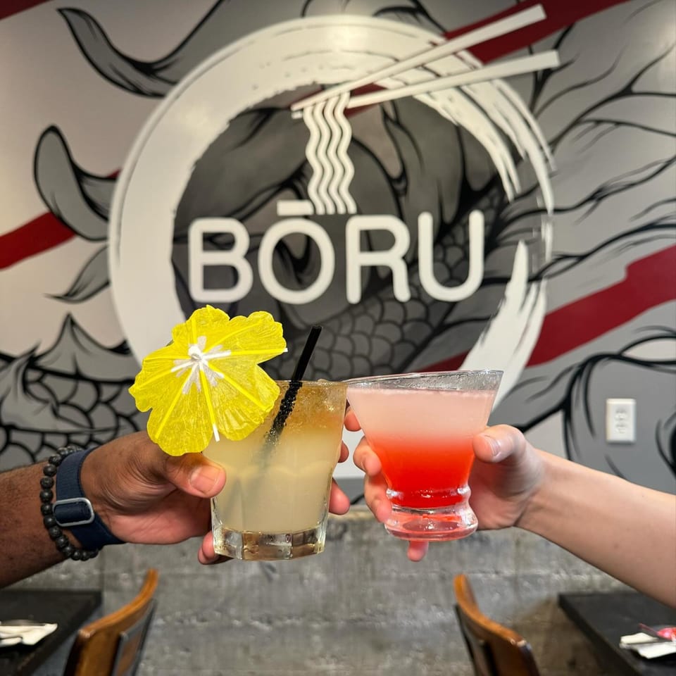 Two hands holding colorful cocktails, one yellow with an umbrella, against a Boru Ramen logo.