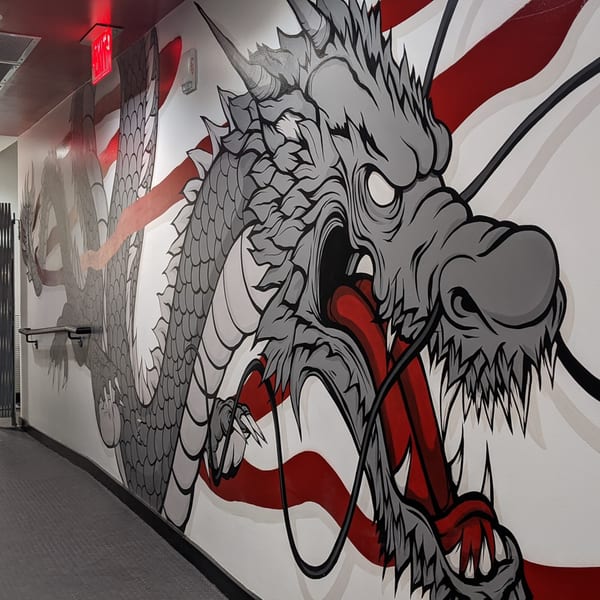 A large, gray and red dragon mural with sharp claws and teeth covers a white wall at Boru Ramen.