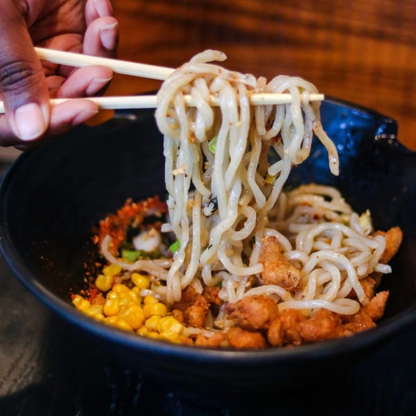 Chopsticks lifting Boru Ramen noodles from a black bowl with corn and chicken.