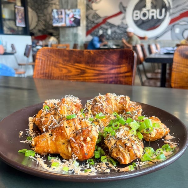 Boru Ramen's fried chicken appetizer, garnished with green onions and sauces, on a dark plate.