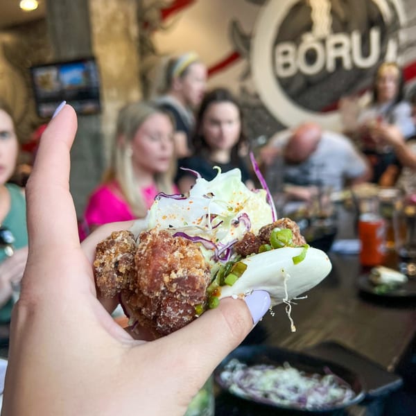 Hand holding a Boru Ramen bao bun with fried chicken, cabbage, and green onions.