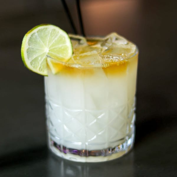 A Boru Ramen cocktail with a lime wedge and ice, featuring a white base and amber top layer.
