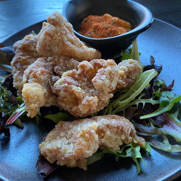 Crispy Japanese karaage chicken pieces on a bed of fresh greens with a side of spice mix.