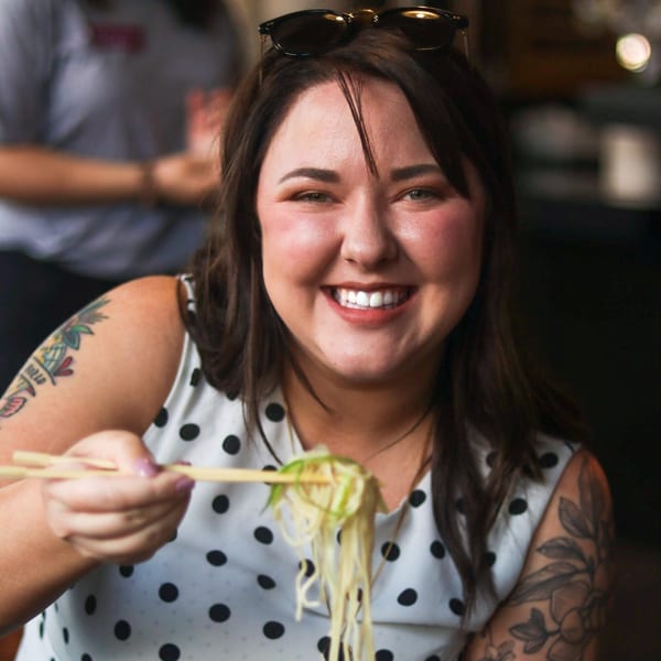 Smiling woman with tattoos eating Boru Ramen noodles with chopsticks.