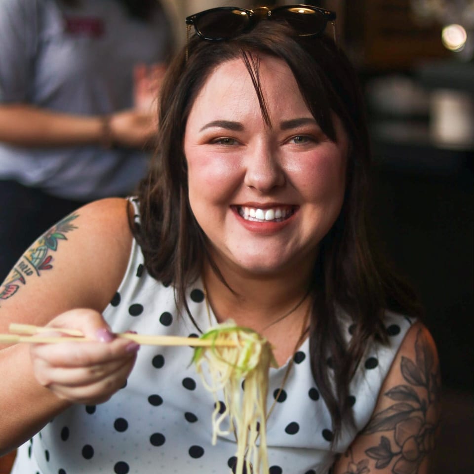 Smiling woman with tattoos eating Boru Ramen noodles with chopsticks.