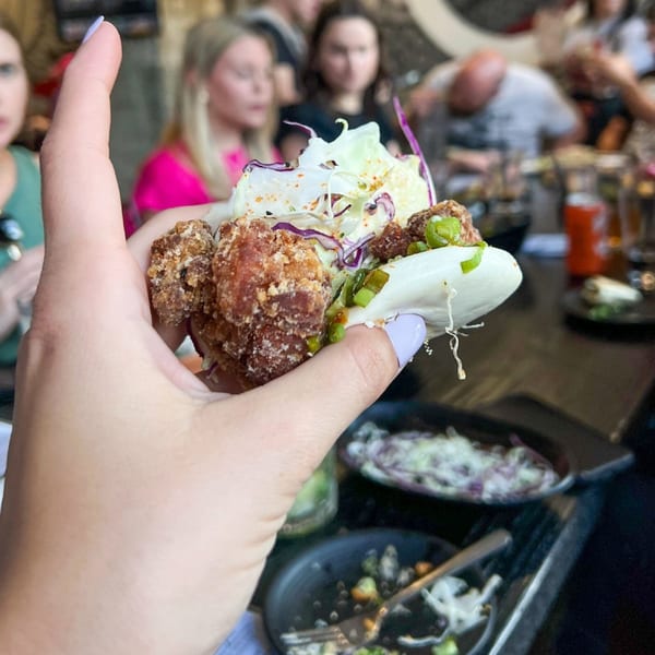 A hand holds a Boru Ramen fried chicken bao bun with cabbage and green onions.