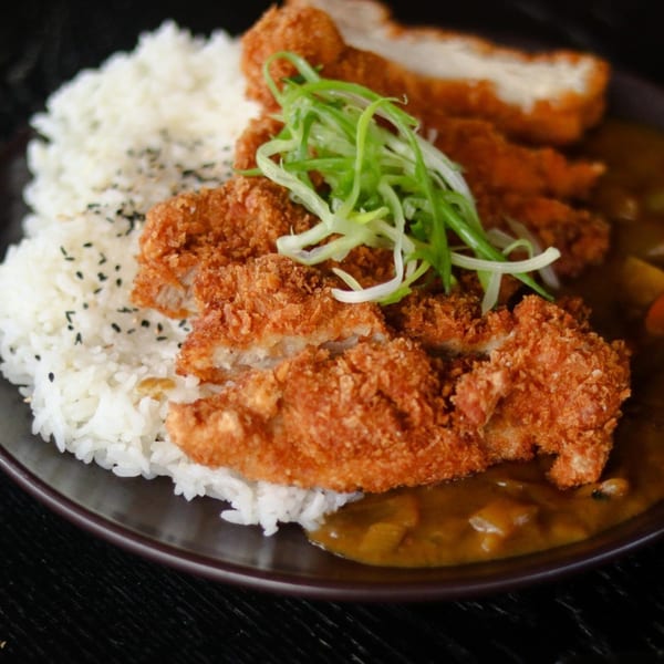 Crispy chicken katsu, white rice with black sesame seeds, and rich curry sauce on a dark plate.